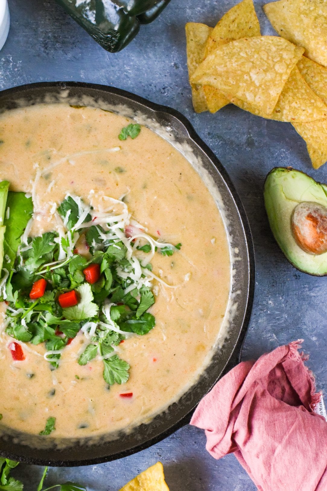beer cheese queso in a cast-iron skillet with chips and avocados sitting on a table