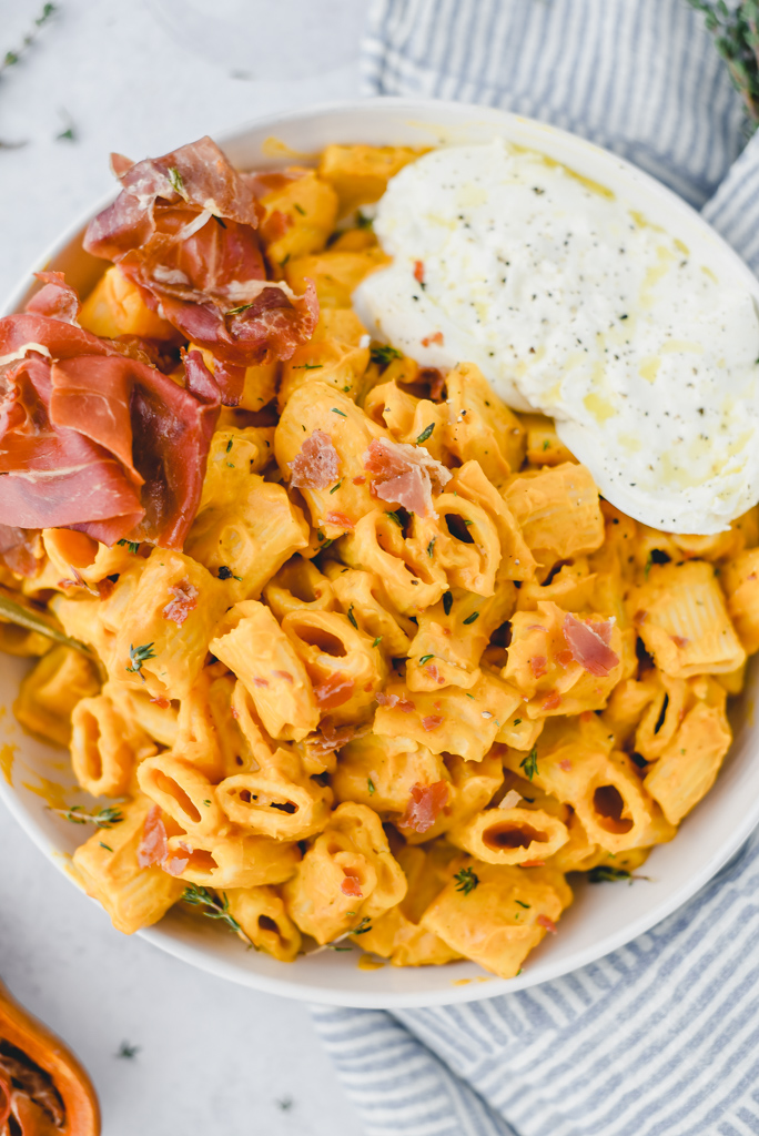 Creamy Honey Nut Squash Pasta in a shallow bowl with crispy prosciutto and burrata cheese on top.