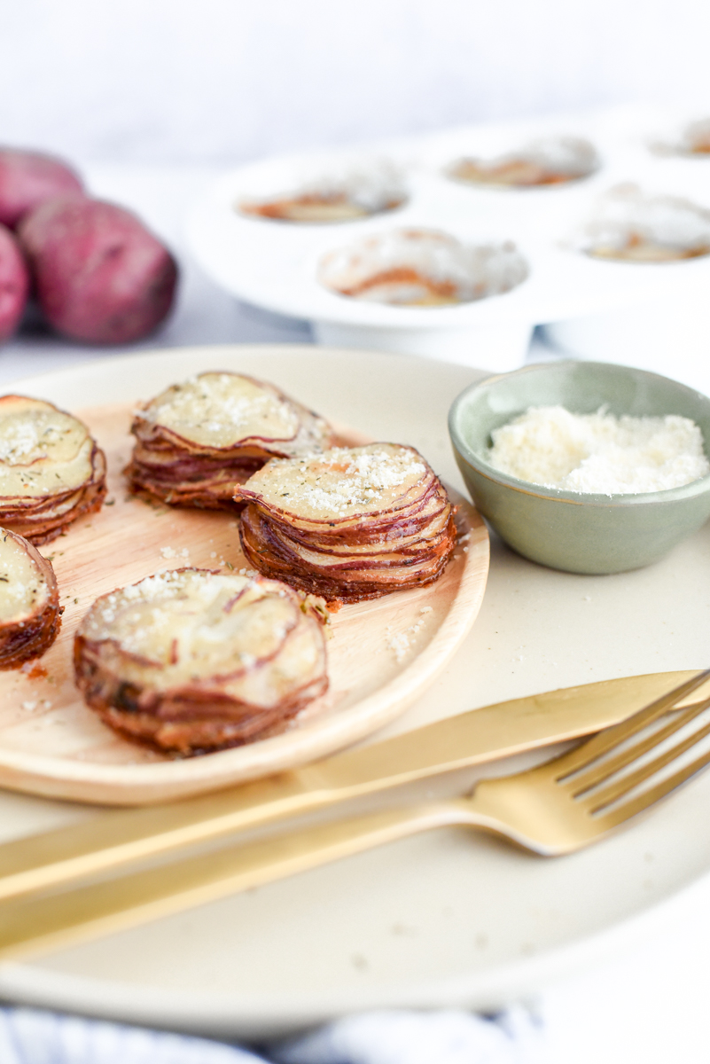 Crispy Garlic Parmesan Potato Stacks on a plate with a small bowl of parmesan and fresh red potatoes in the corner