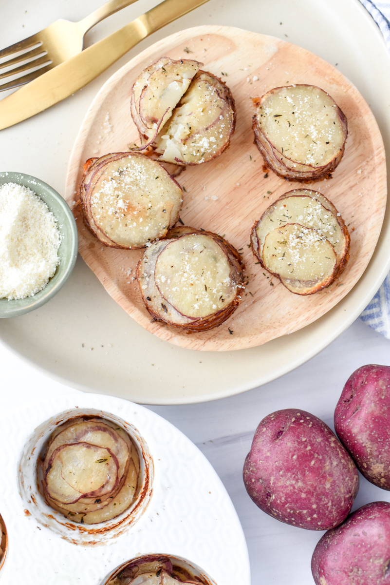 Crispy Garlic Parmesan Potato Stacks on a plate with a small bowl of parmesan and fresh red potatoes in the corner