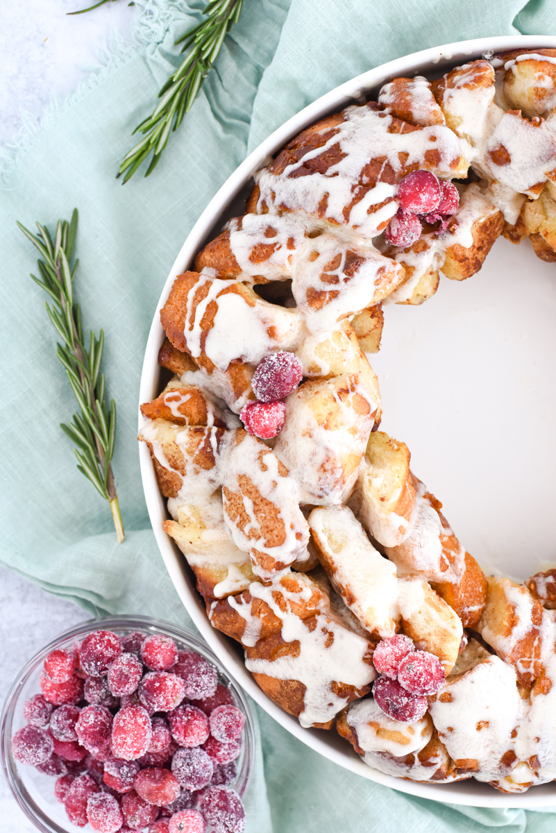Monkey Bread in a ring with eggnog frosting drizzled over the top surrounded by sugared cranberries, rosemary and eggnog.