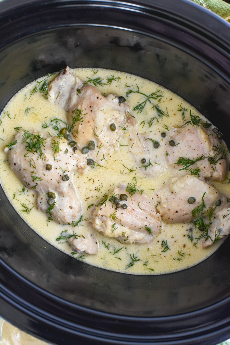 chicken dijon sitting in slow cooker with juices, capers, and dill