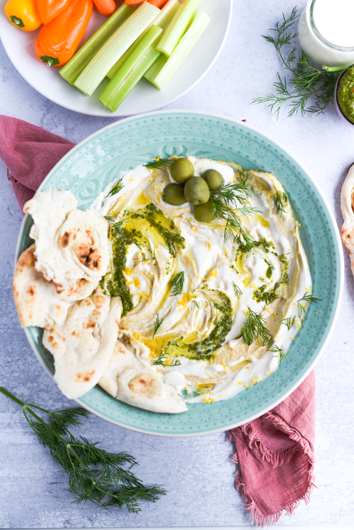Creamy Hummus with Whipped Feta Dip with pita, olive oil, pesto, and olives for garnish in a dipping bowl