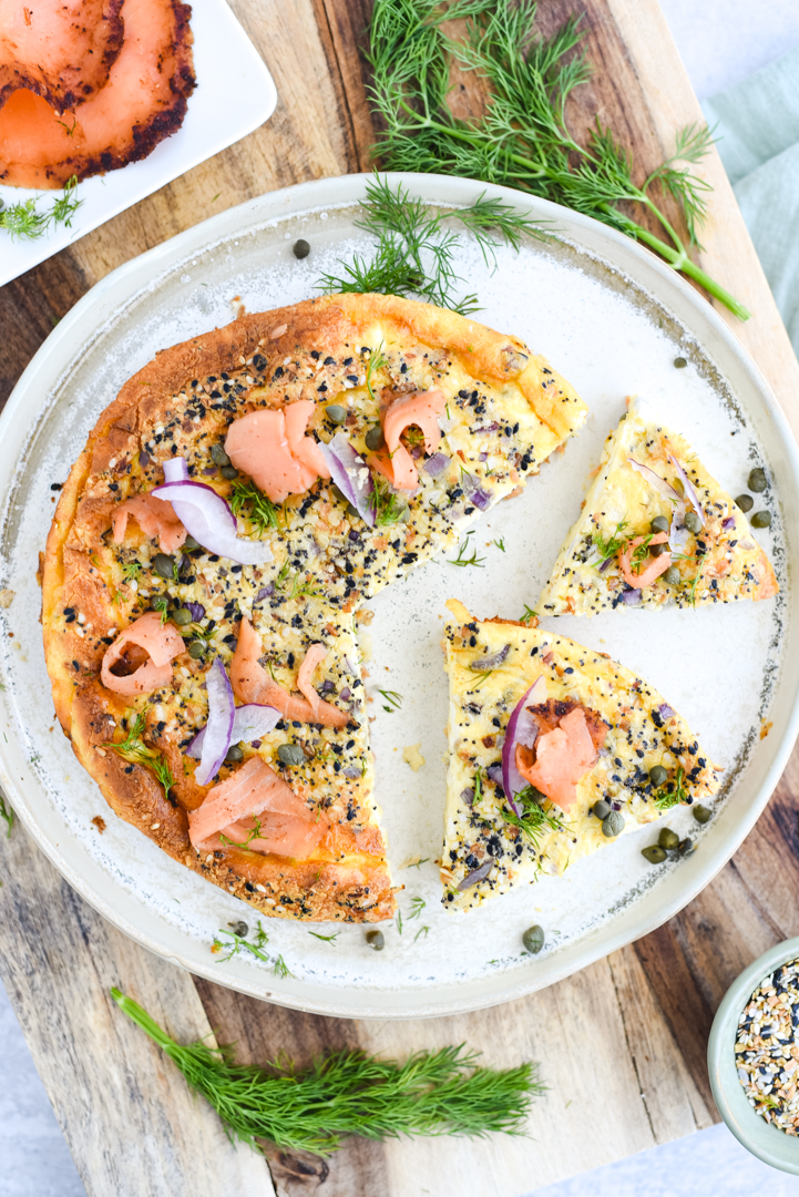 sliced quiche on a plate with salmon, onion, capers, and everything seasoning for garnish