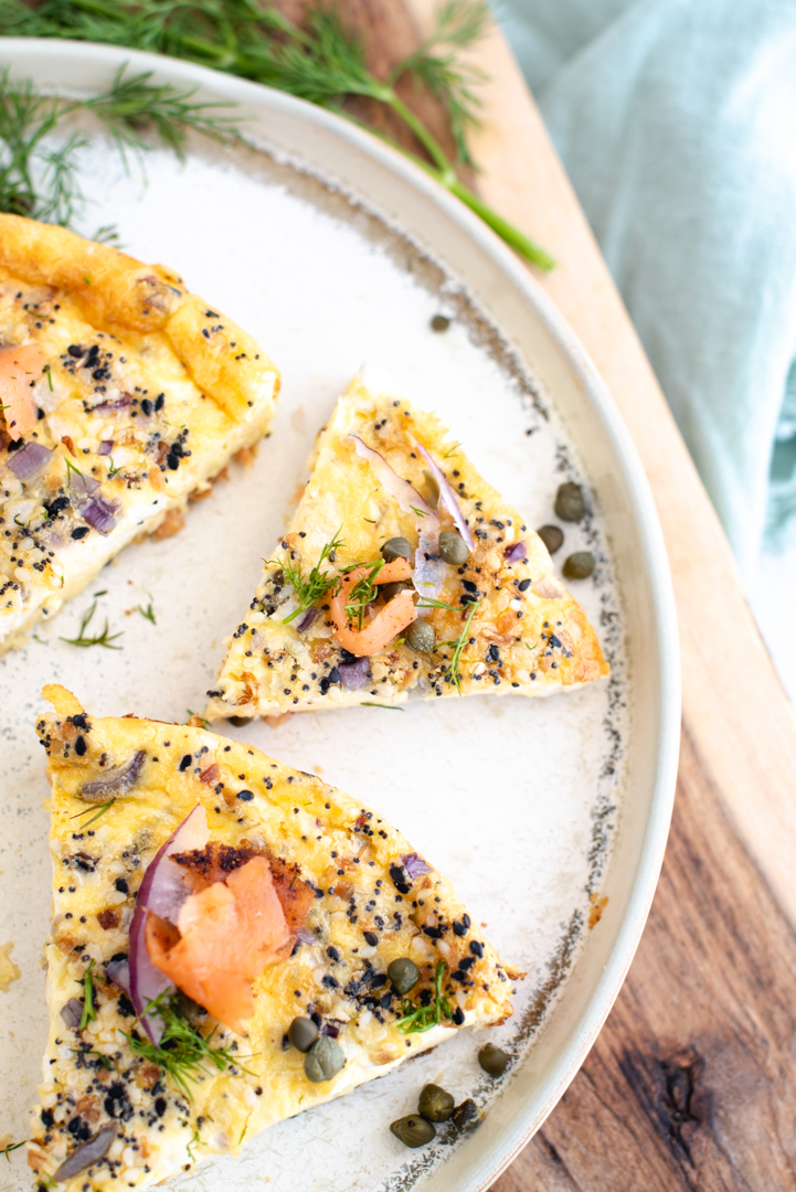 sliced quiche on a plate with salmon, onion, capers, and everything seasoning for garnish